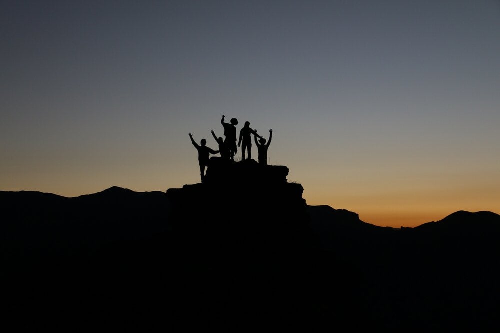 Silhouette of people standing on mountain during a sunrise.